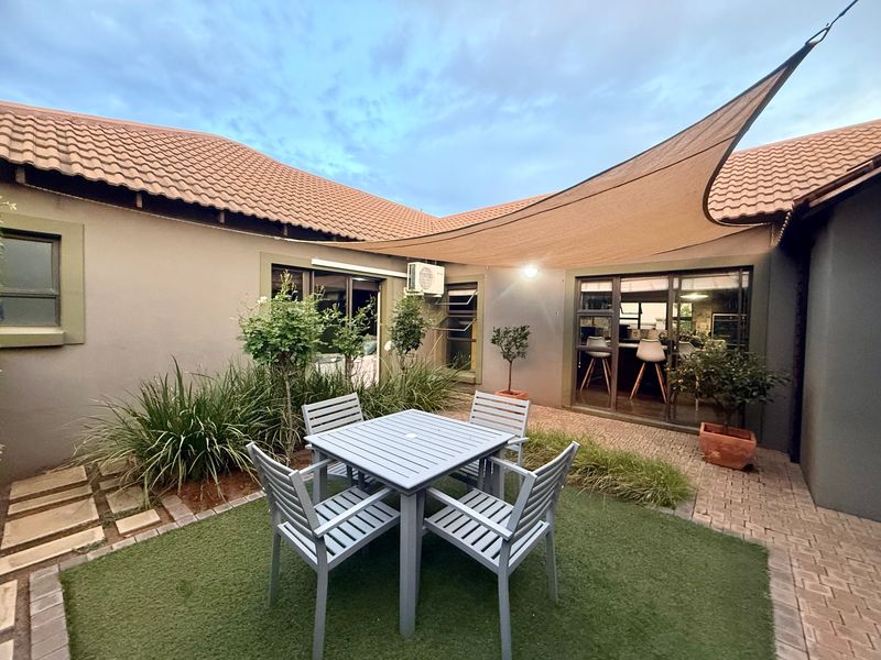 A well-maintained paved patio area featuring an artificial lawn, shade sail, and direct access to the interior through sliding glass doors.