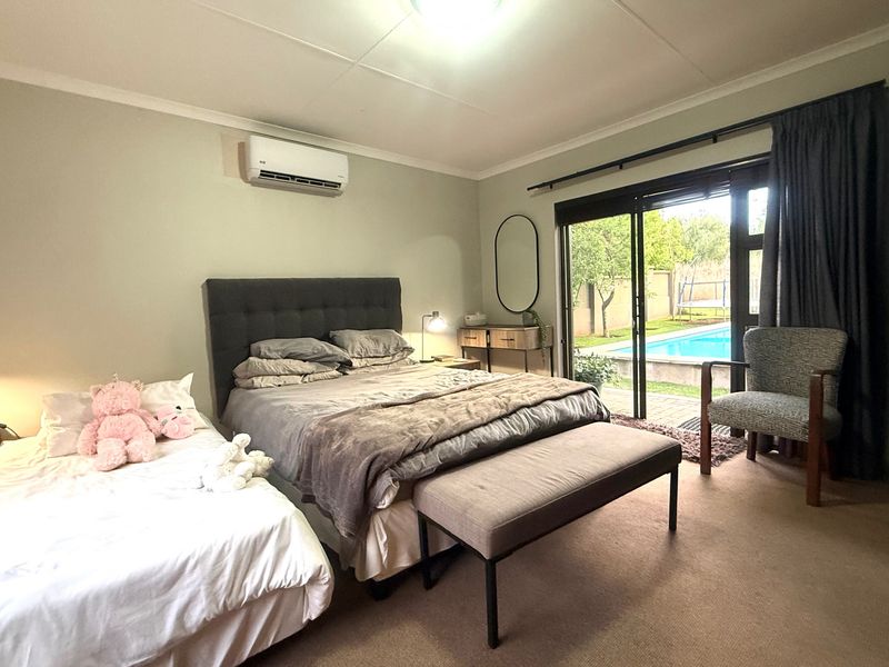 Spacious bedroom featuring a split-system air conditioner, carpeted flooring, and direct access to the outdoor pool area through sliding glass doors.