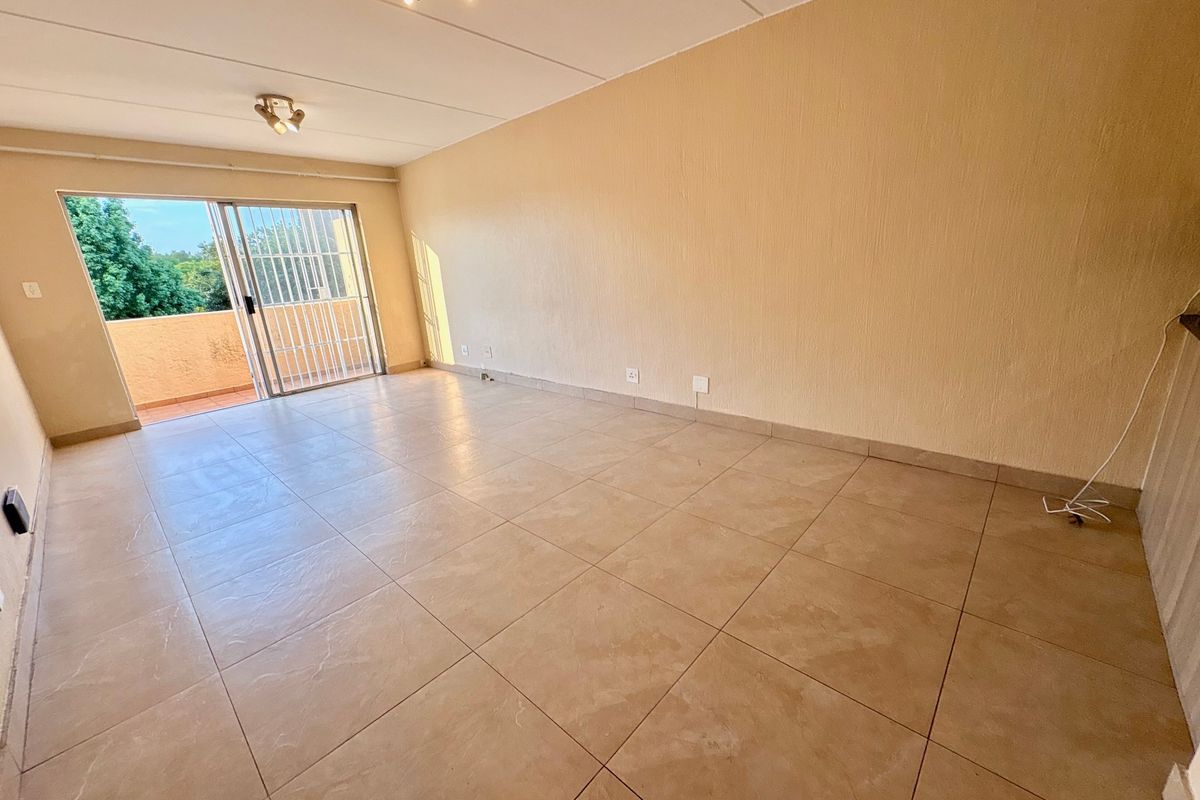 A spacious, empty living room featuring tiled flooring and a sliding glass door that opens onto a balcony, providing natural light.