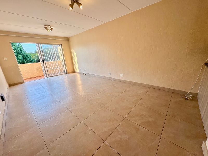 A spacious, empty living room featuring tiled flooring and a sliding glass door that opens onto a balcony, providing natural light.