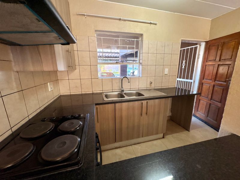 A functional kitchen featuring granite countertops, built-in cabinetry, an electric hob with extractor fan, and a double basin sink with tiled backsplash.