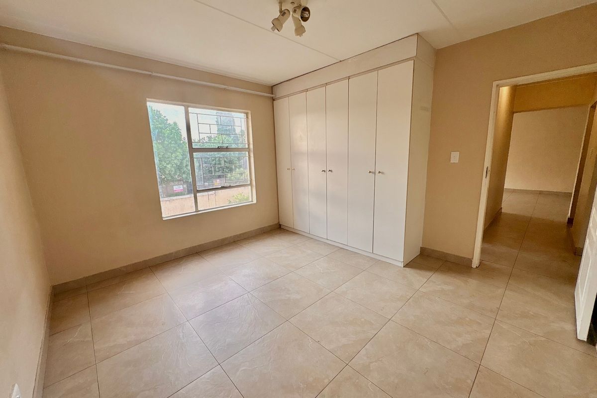 A vacant bedroom featuring neutral tiled flooring, built-in storage cupboards, and a window with security bars.