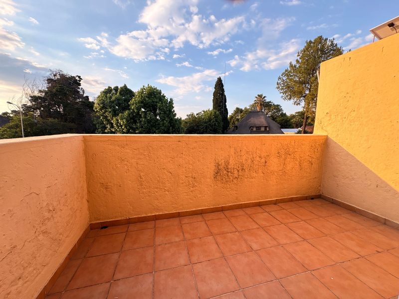An open-air balcony featuring terracotta floor tiles and a plastered masonry balustrade with views of the surrounding neighborhood.