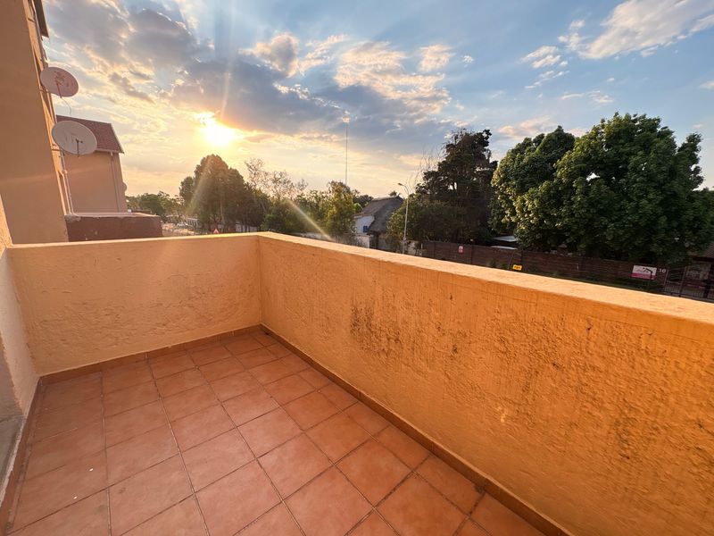 An open-air balcony featuring tiled flooring and a masonry balustrade, offering an elevated view of the surrounding neighborhood at sunset.