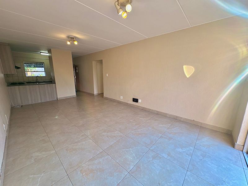 An open-plan living and kitchen area featuring neutral tiled flooring, built-in cabinetry, and a functional layout suitable for modern living.