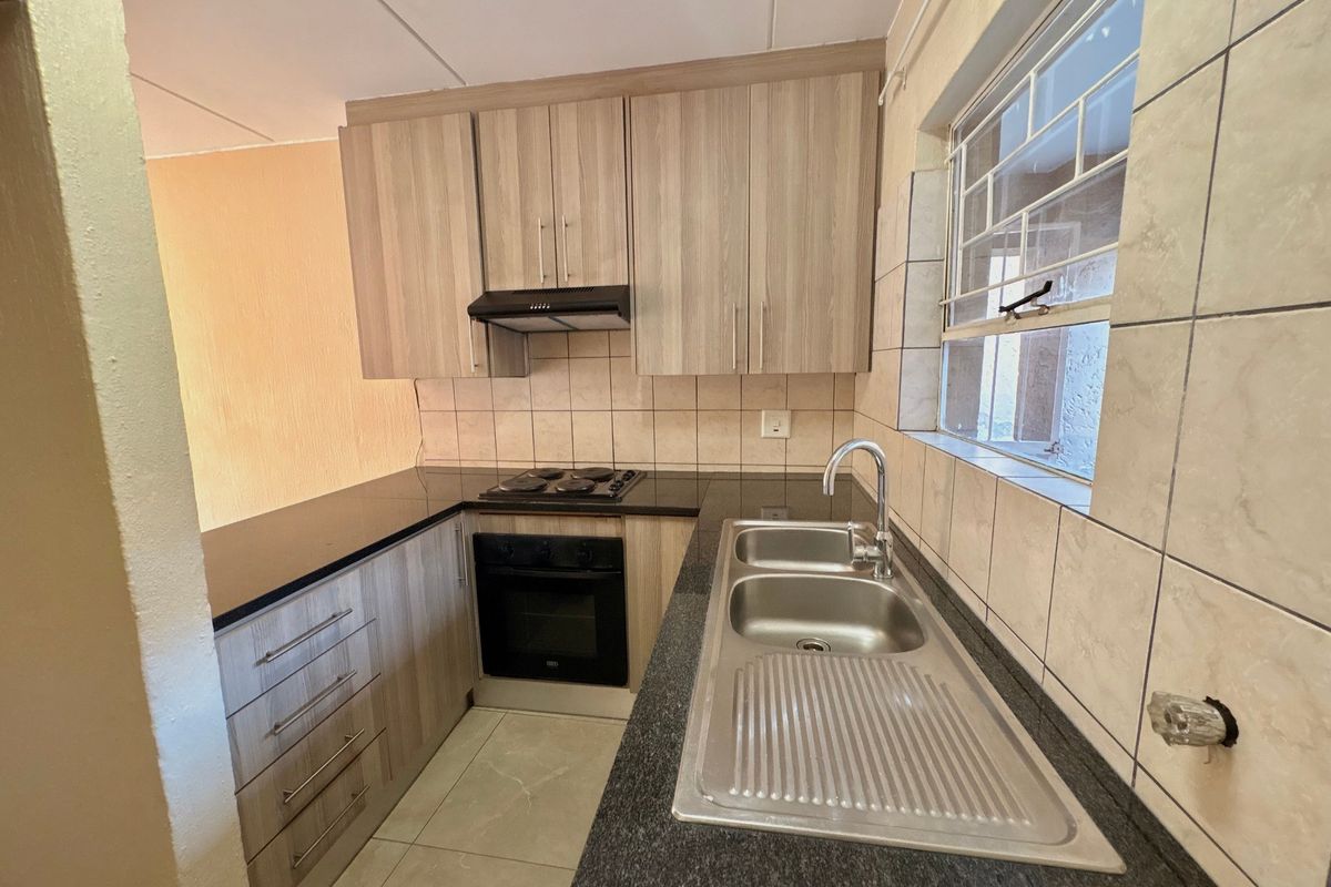 A functional kitchen featuring wood-look cabinetry, dark countertops, built-in oven and hob, and a stainless steel sink with tiled backsplash.