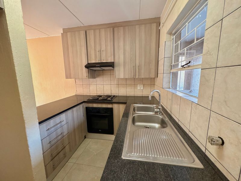 A functional kitchen featuring wood-look cabinetry, dark countertops, built-in oven and hob, and a stainless steel sink with tiled backsplash.