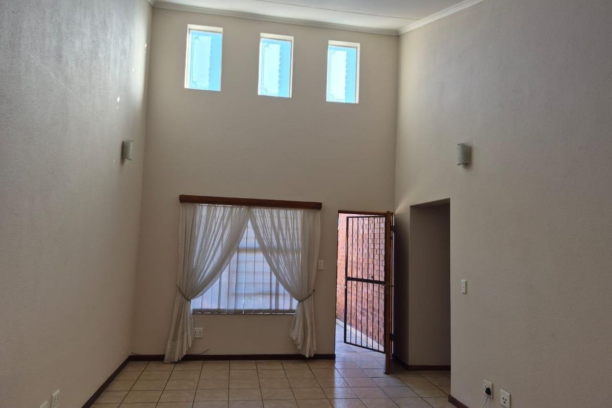 Spacious living area featuring high ceilings, tiled flooring, and abundant natural light from clerestory windows, with direct access to an outdoor area.