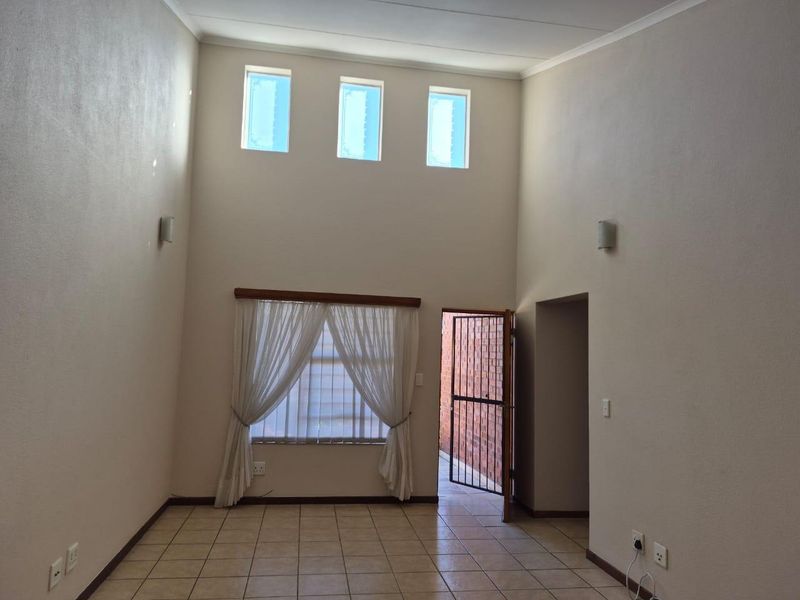 Spacious living area featuring high ceilings, tiled flooring, and abundant natural light from clerestory windows, with direct access to an outdoor area.