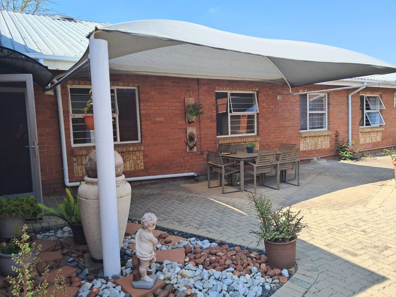A paved outdoor patio area featuring a shade sail, brick exterior walls, and aluminium windows, providing a functional space for outdoor dining.