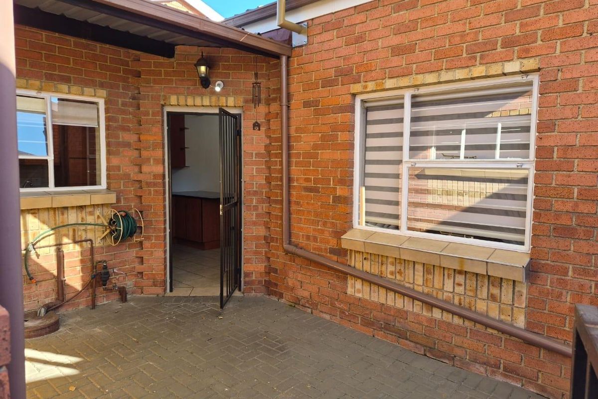 A paved rear courtyard area featuring exposed brick walls, a security gate entrance, and functional downpipes, providing a practical outdoor utility space.