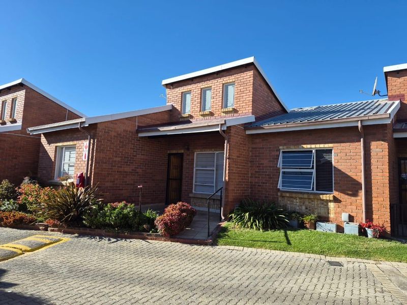 Front elevation of a face brick townhouse featuring a paved driveway, landscaped garden, and secure entrance.