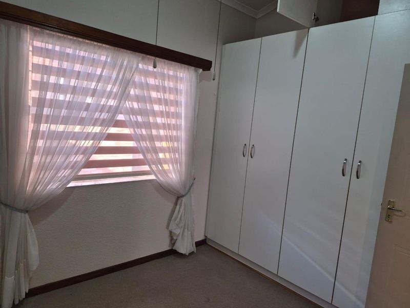 A clean, empty bedroom featuring neutral carpeted flooring and ample built-in cupboard storage space.