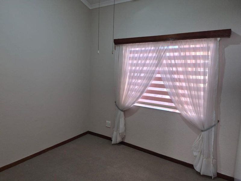 A clean, empty bedroom featuring neutral wall tones, carpeted flooring, and a window fitted with a timber pelmet and dual-layer blinds.