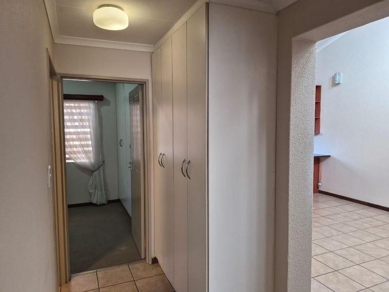 A functional hallway featuring built-in storage cupboards, tiled flooring, and an open archway leading into the adjacent living area.