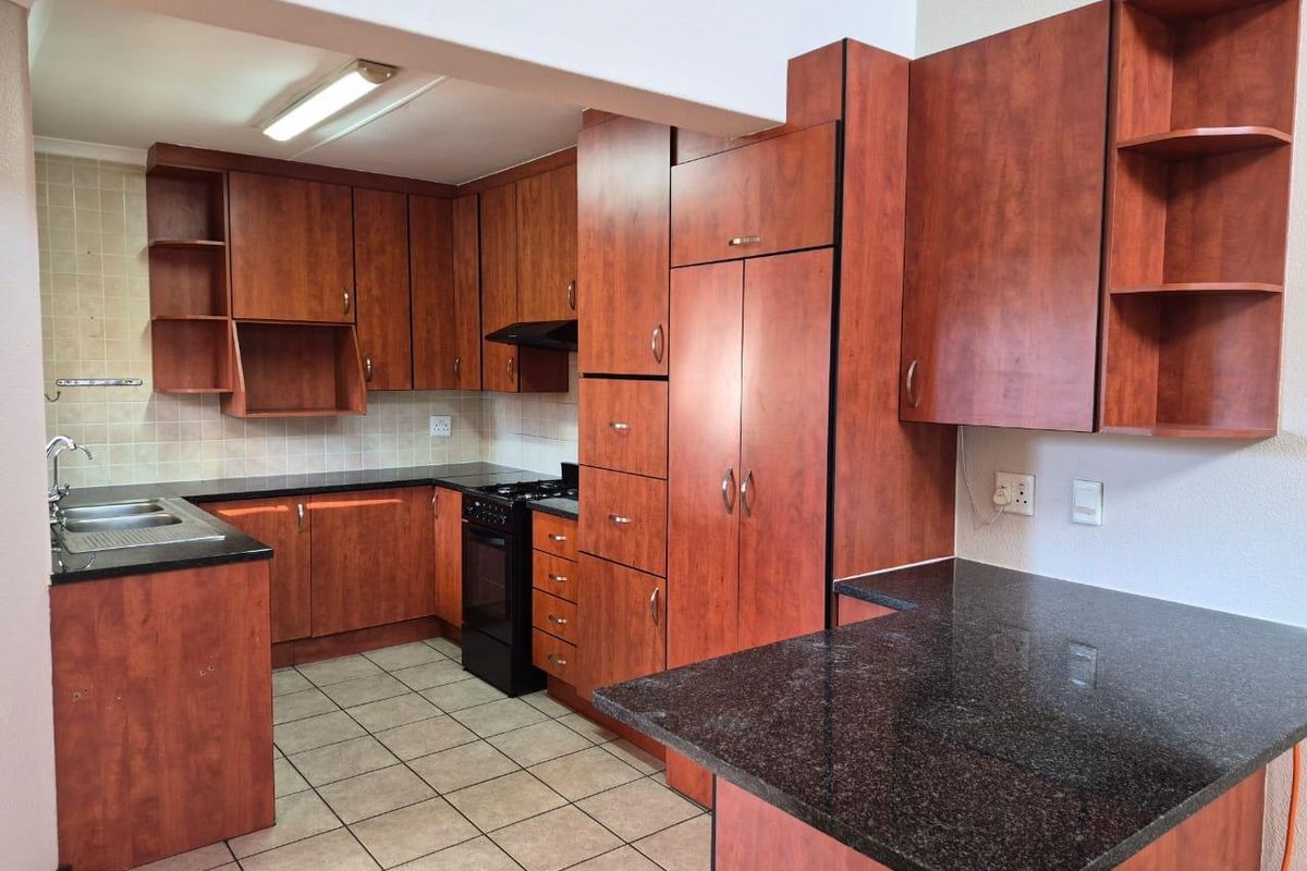 A functional kitchen featuring dark wood-look cabinetry, granite countertops, tiled flooring, and a built-in stove with an extractor fan.