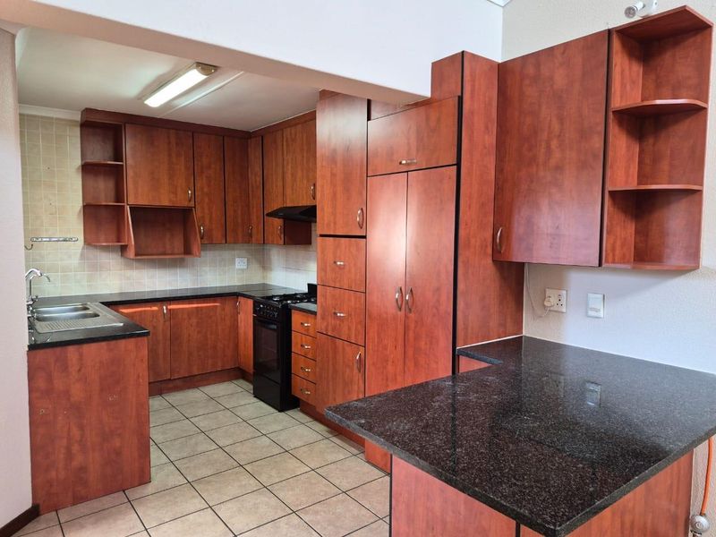 A functional kitchen featuring dark wood-look cabinetry, granite countertops, tiled flooring, and a built-in stove with an extractor fan.