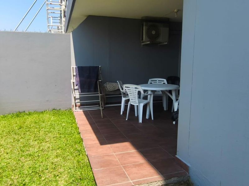 Covered patio area featuring tiled flooring and a built-in braai, overlooking a small private garden space.