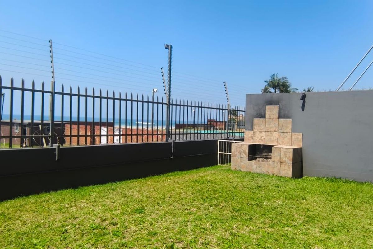 A private garden area featuring a built-in braai, tiled patio space, and secure perimeter wall with electric fencing, offering views towards the coast.