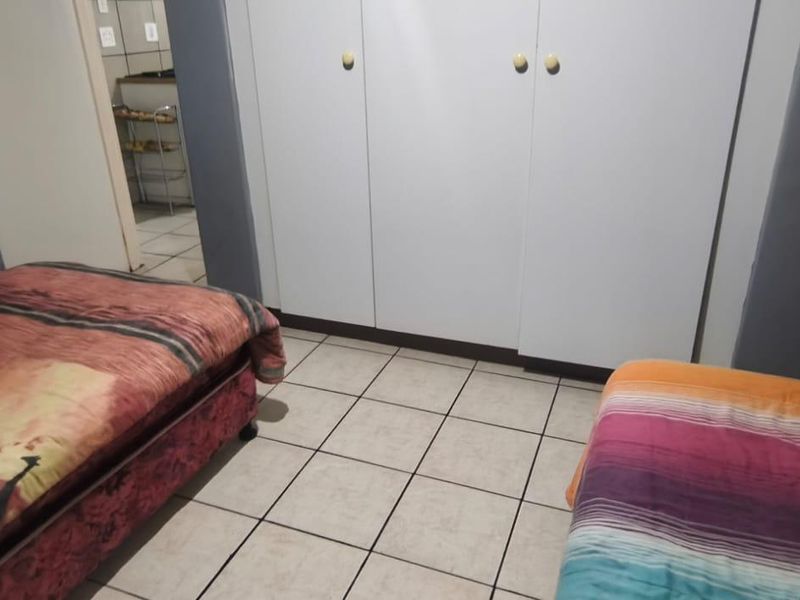 A bedroom featuring tiled flooring and built-in cupboards, with a view leading into an adjacent tiled area.