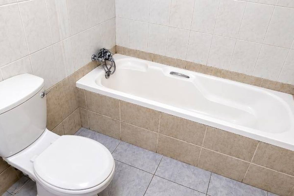 A functional bathroom featuring a built-in bathtub and toilet with neutral wall and floor tiling.