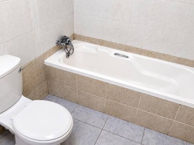 A functional bathroom featuring a built-in bathtub and toilet with neutral wall and floor tiling.
