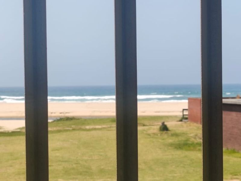 A view of the beach and ocean framed by metal security bars from an elevated position.