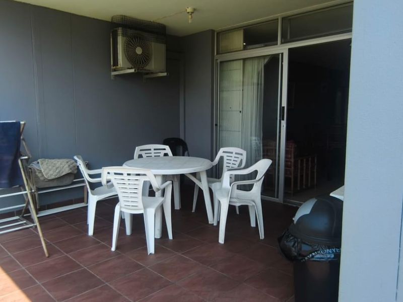 A covered patio area featuring tiled flooring and a sliding glass door entrance, providing a functional outdoor space for the apartment.