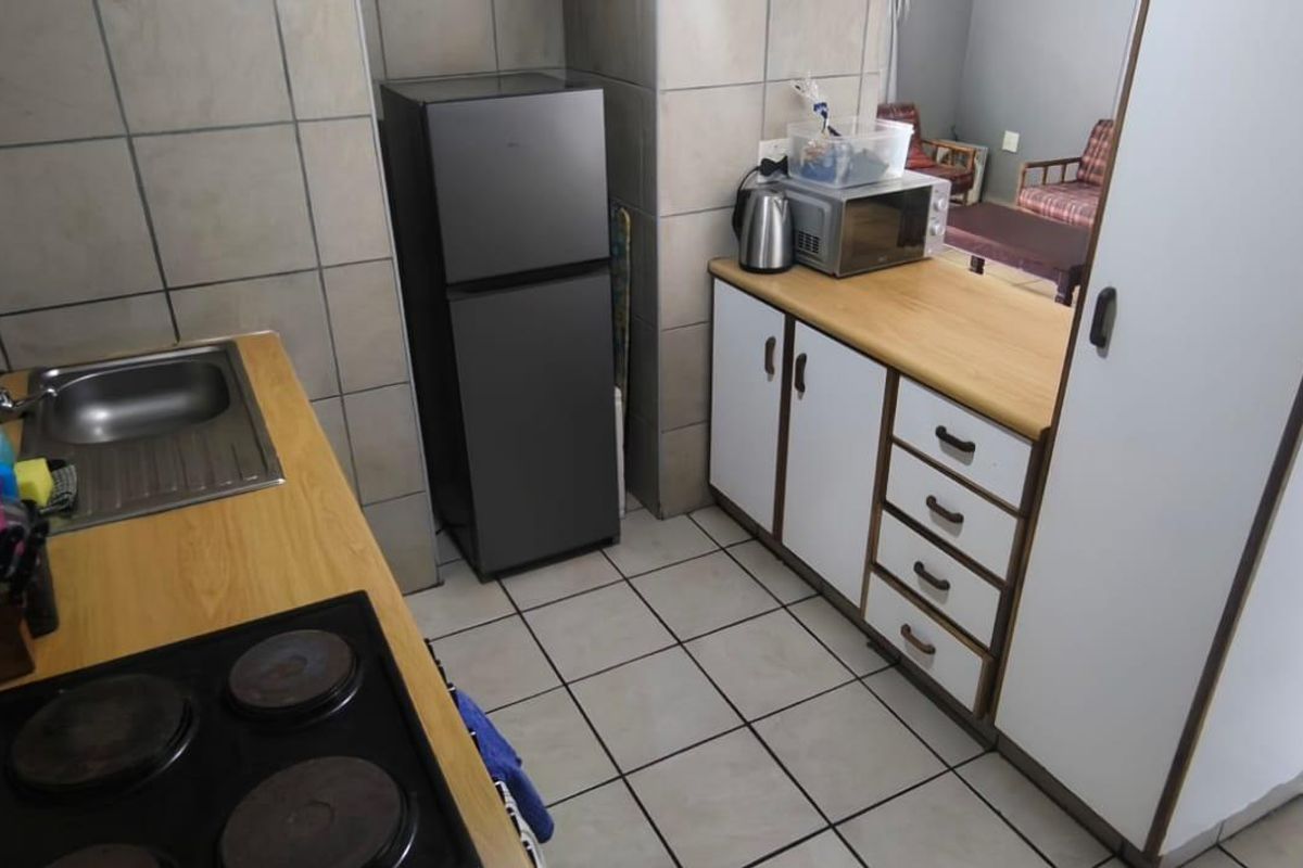 Compact kitchen featuring laminate countertops, built-in cabinetry, a stainless steel sink, and an electric hob with tiled splashbacks and flooring.
