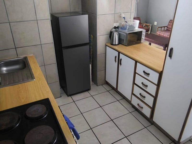 Compact kitchen featuring laminate countertops, built-in cabinetry, a stainless steel sink, and an electric hob with tiled splashbacks and flooring.