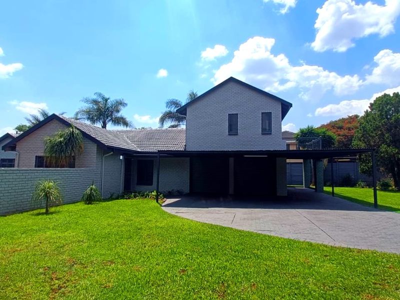 Front view of a double-story brick house featuring a paved driveway, integrated carport, and well-maintained front lawn.