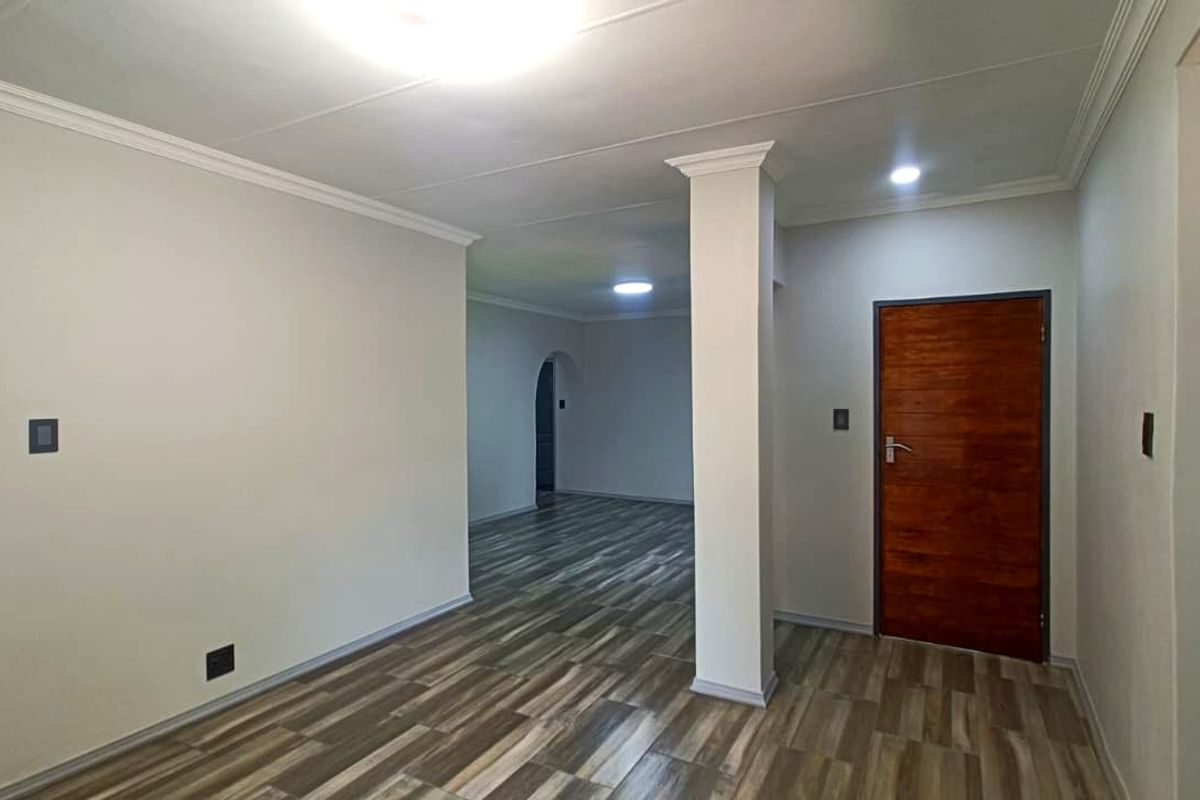 A bright, open-plan living area featuring modern wood-look laminate flooring, neutral walls, and a structural column, providing a clean and versatile space.