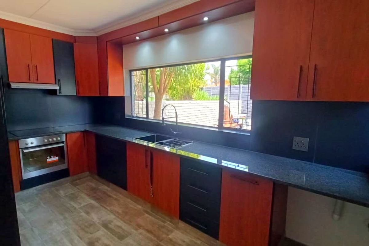 Modern kitchen featuring two-tone cabinetry, granite countertops, built-in oven, extractor fan, and a large window overlooking the garden.