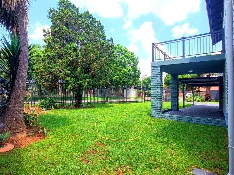 A well-maintained rear garden featuring a lawn, a paved patio area, and an elevated balcony with metal railings attached to the brick house structure.
