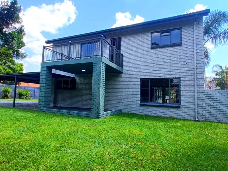 Rear view of a two-story house featuring a painted brick facade, a balcony with metal railings, and an attached carport.