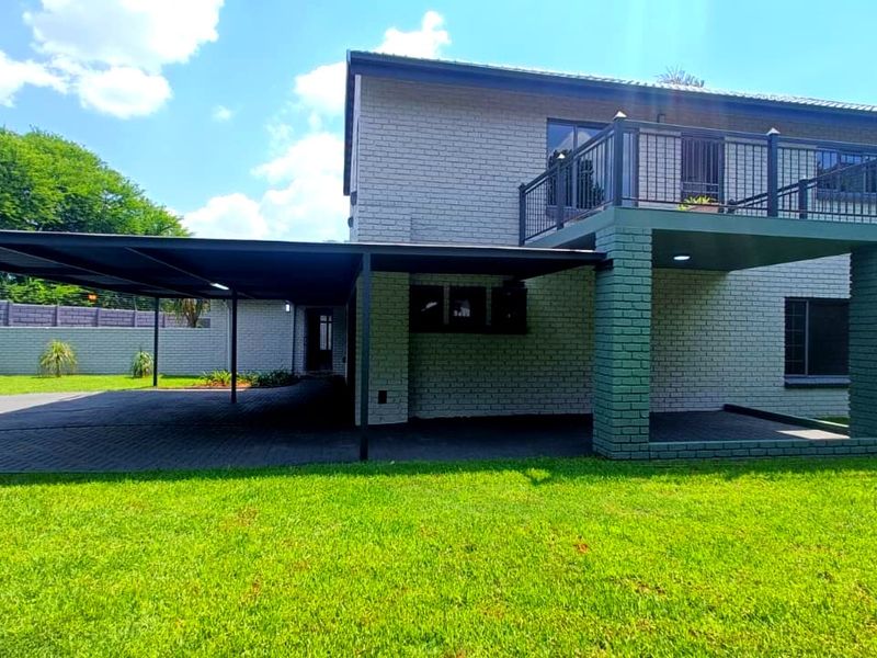 Rear view of a two-story brick house featuring a large covered carport, a spacious upper-level balcony, and a well-maintained lawn.