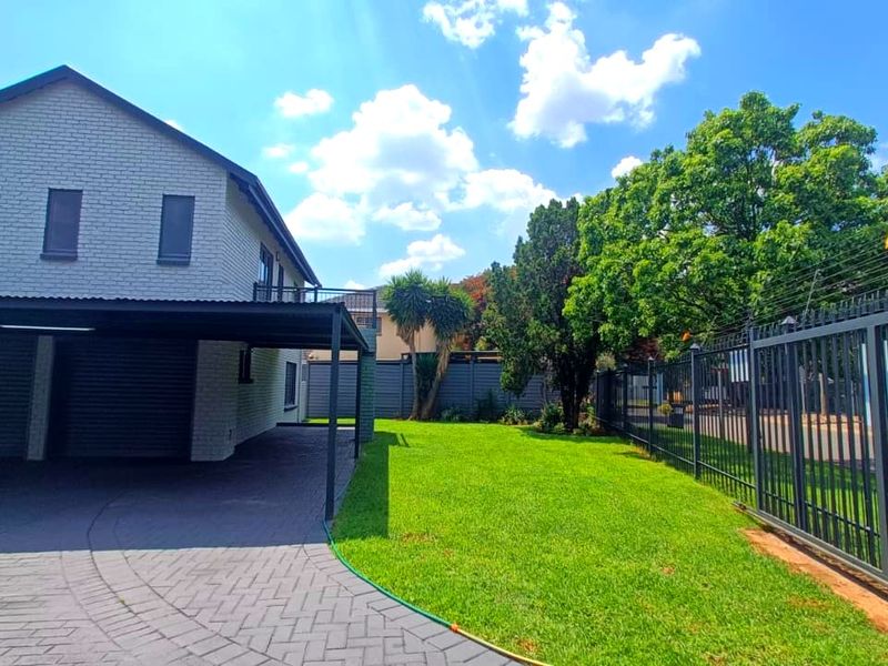 Front view of the property featuring a paved driveway, covered carport, well-maintained lawn, and secure perimeter fencing with electric security wires.