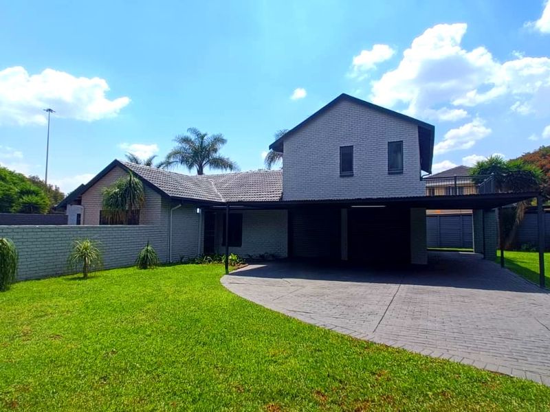 Front view of a well-maintained house featuring a brick facade, tiled roof, paved driveway, and a spacious carport set within a landscaped garden.