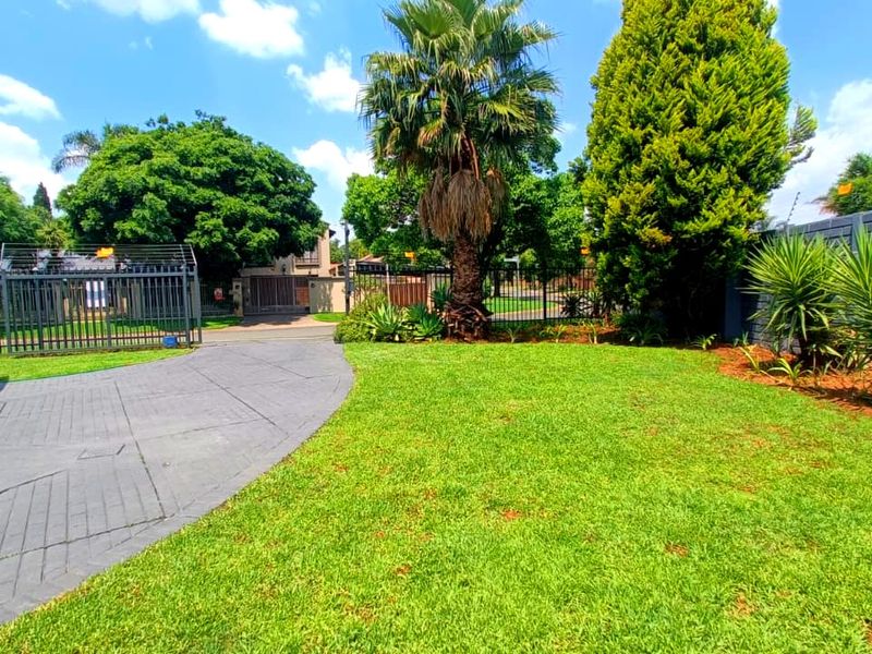 A well-maintained front garden area featuring a paved driveway, established landscaping, and secure perimeter fencing with electric security wires.