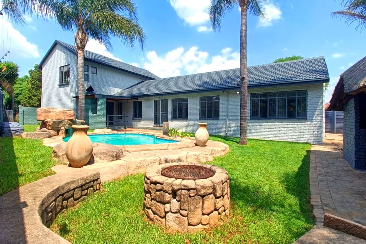 Rear exterior view featuring a swimming pool, stone fire pit, landscaped garden, and a thatched lapa area, perfect for outdoor entertaining.