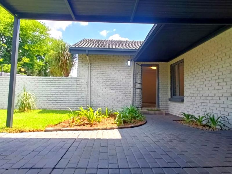 A well-maintained front entrance featuring a covered carport, paved driveway, and a secure, neatly landscaped garden with perimeter walling and electric fencing.