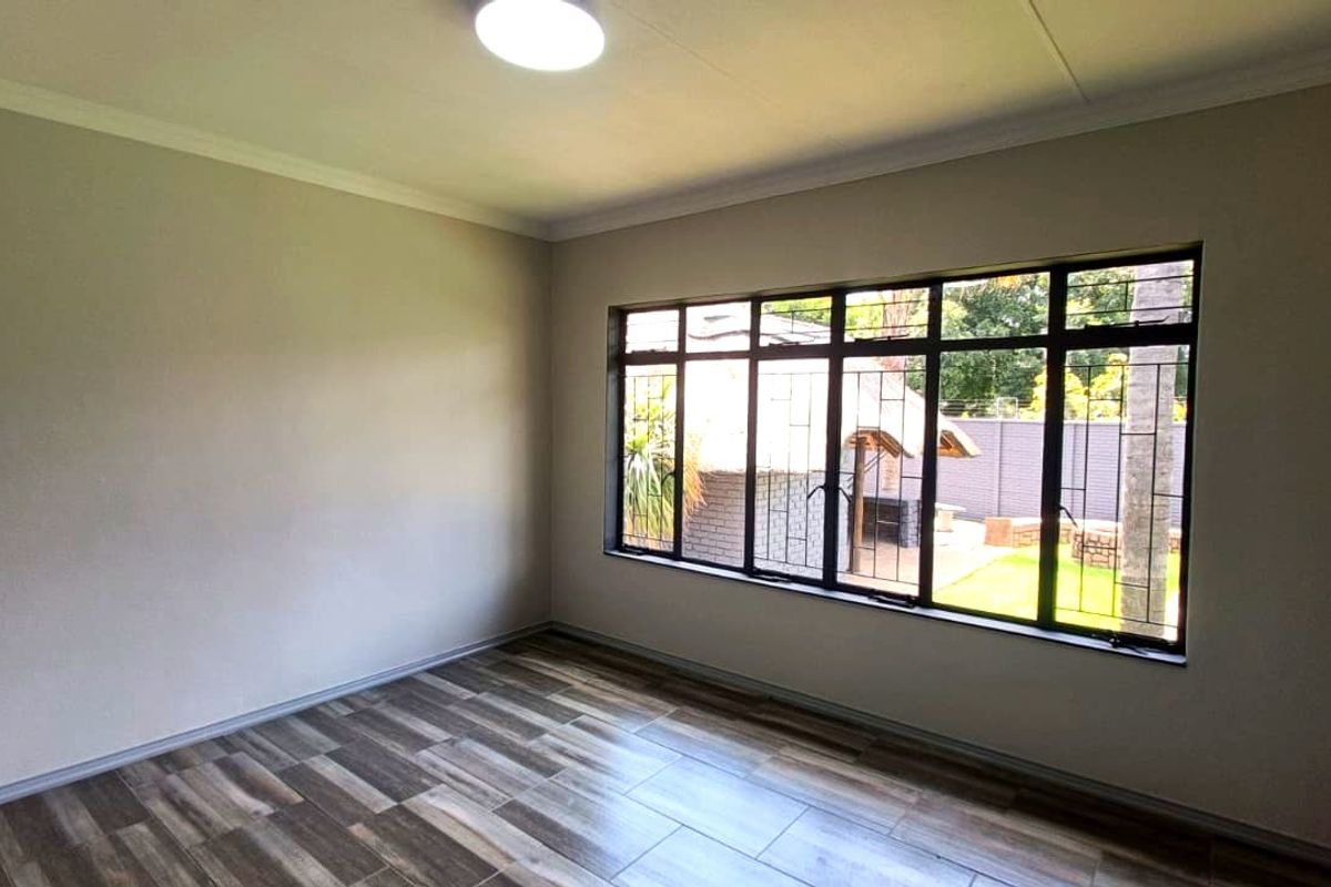 A bright, empty bedroom featuring modern wood-look tiled flooring, large windows with security bars, and neutral wall finishes.