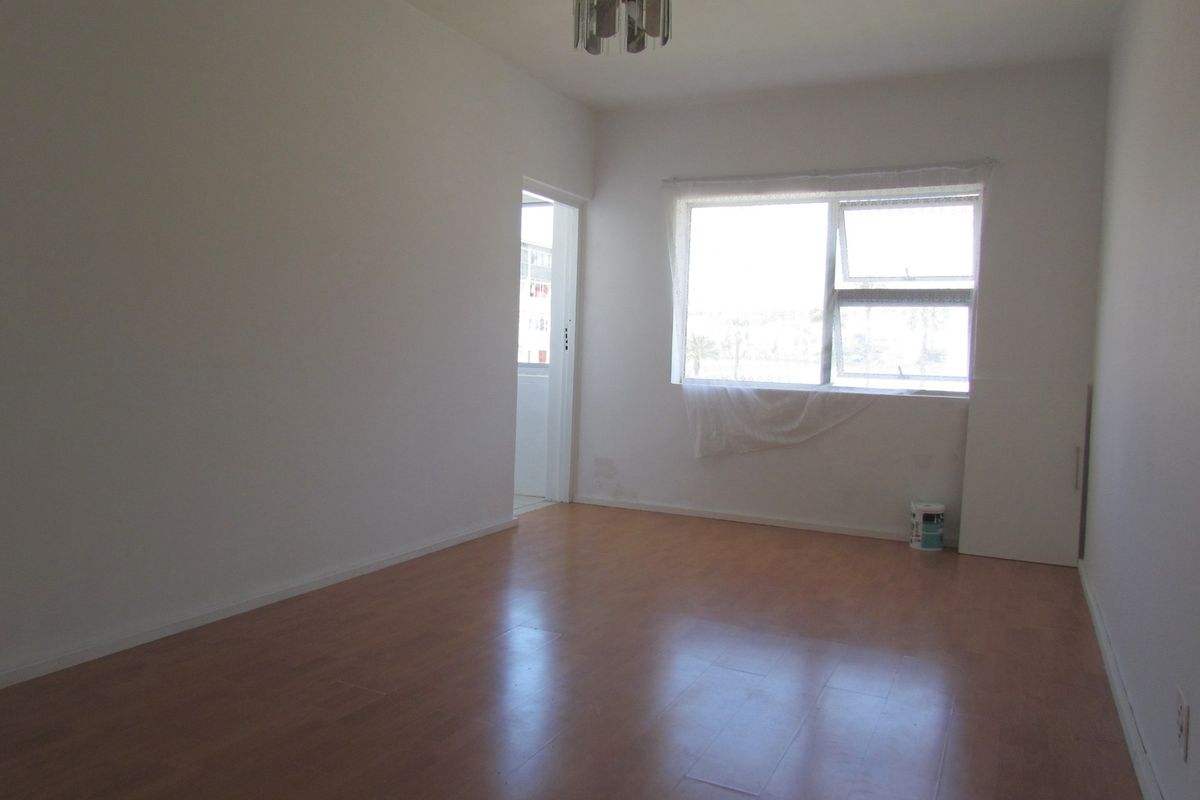 An empty living room featuring laminate flooring and a large window, providing a blank canvas for potential interior design updates.