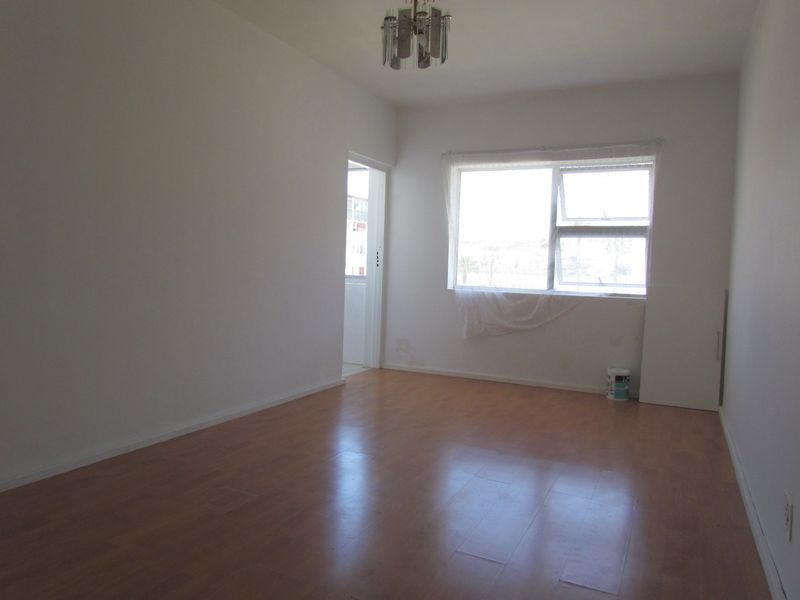 An empty living room featuring laminate flooring and a large window, providing a blank canvas for potential interior design updates.