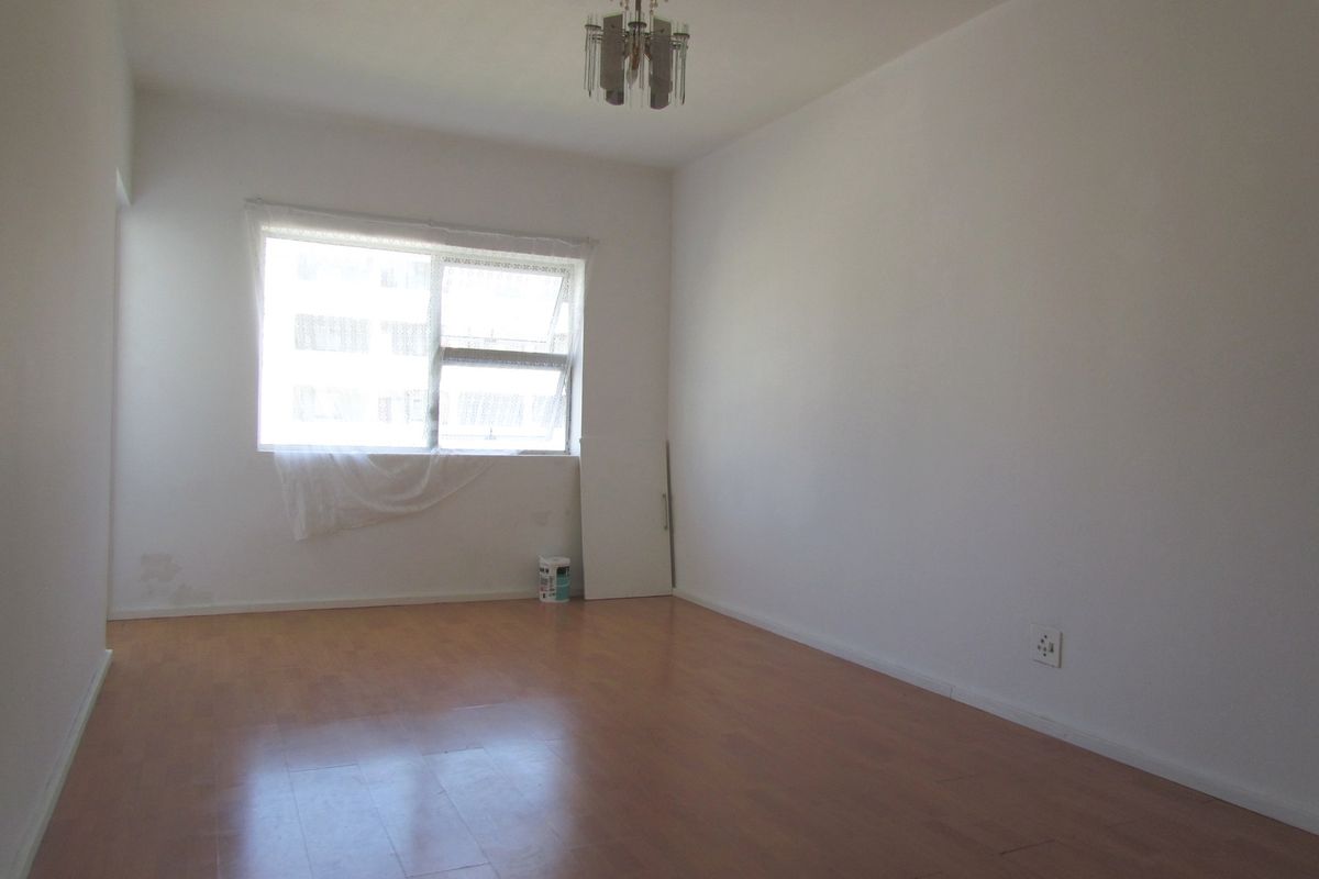An empty bedroom featuring laminate flooring, a central ceiling light fixture, and a window with natural light.