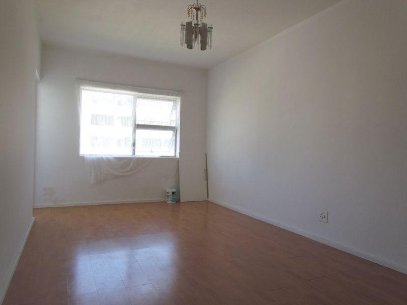 An empty bedroom featuring laminate flooring, a central ceiling light fixture, and a window with natural light.