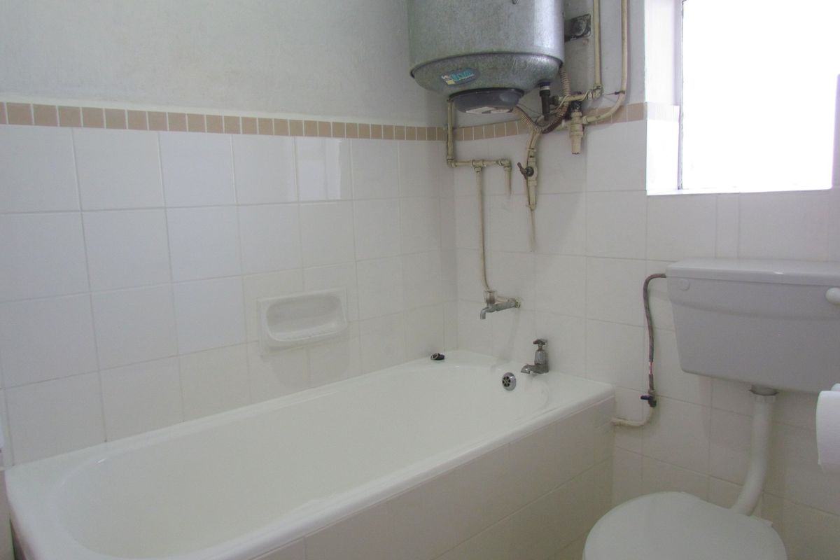 A functional bathroom featuring a standard bathtub, toilet, and wall-mounted electric water heater with exposed plumbing.