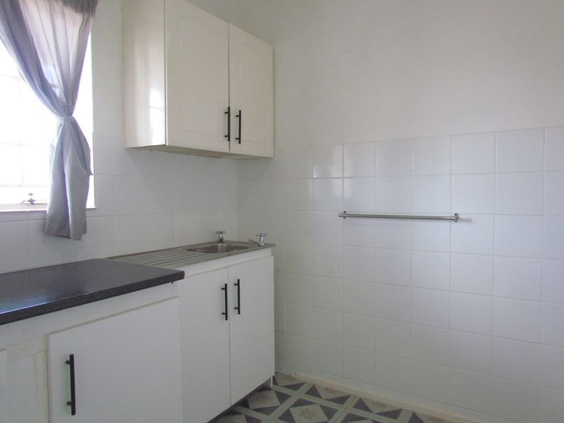 A functional laundry area featuring built-in white cabinetry, a stainless steel sink, tiled splashbacks, and patterned floor tiles.