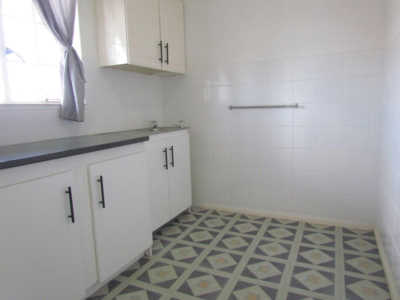 A functional laundry room featuring built-in white cabinetry, a stainless steel sink, tiled splashbacks, and patterned floor tiles.