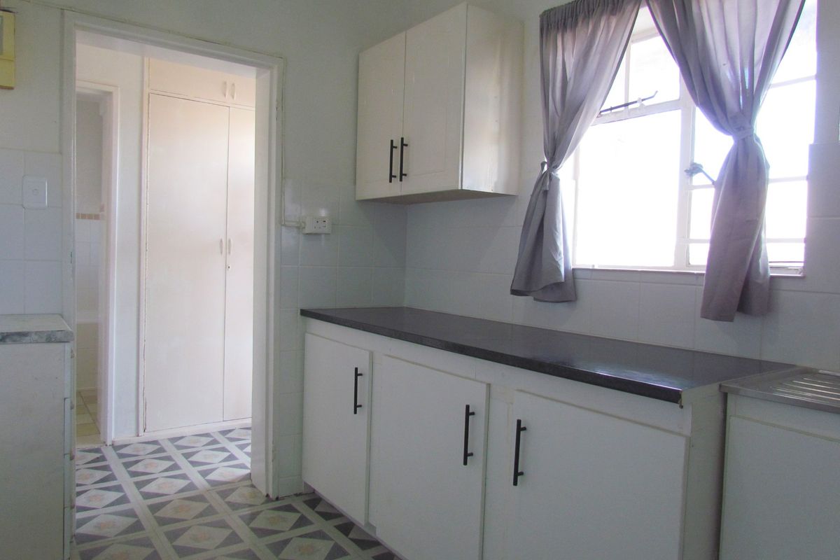 A functional kitchen featuring white built-in cabinetry, dark laminate countertops, tiled splashbacks, and patterned floor tiles, leading into a hallway with built-in storage.
